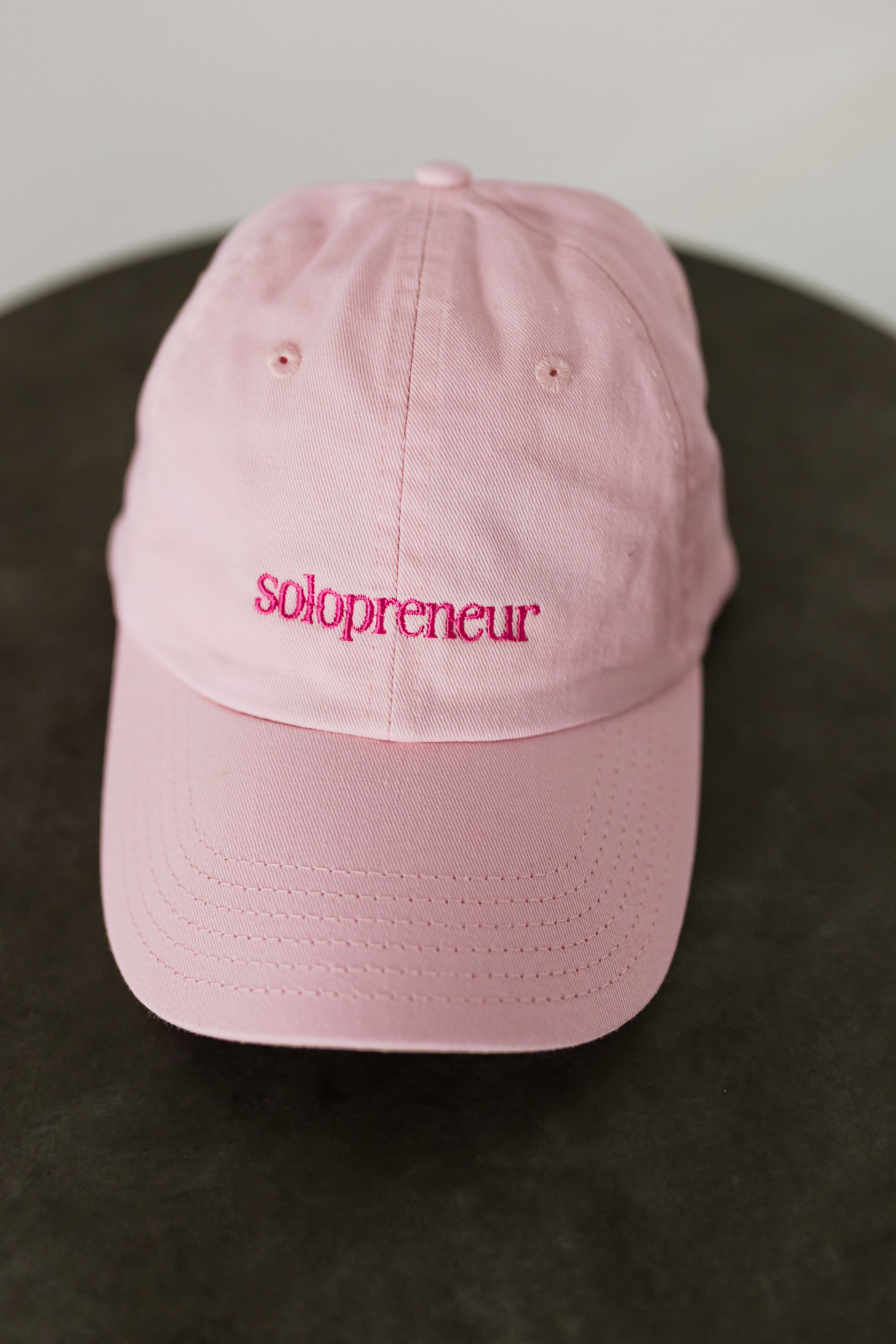 pink baseball cap embroidered with "Solopreneur" on a table